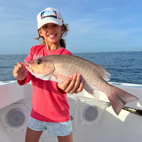 Smiling girl holding up a mutton snapper she caught