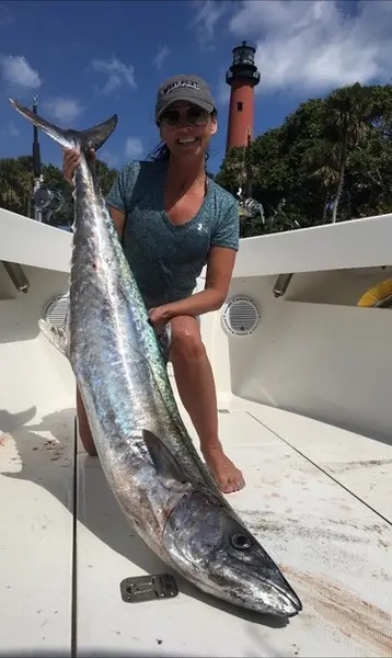 Woman holding a kingfish with the Jupiter Lighthouse in the background